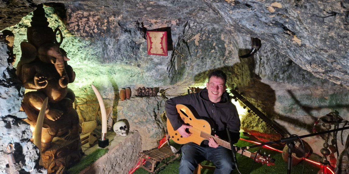 Néma sentado en la cueva de Stone Cage records con su guitarra en las manos.